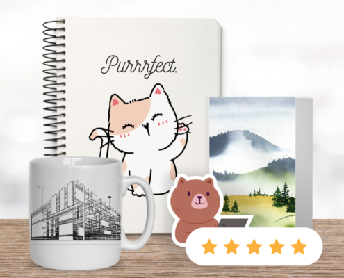 a spiral notebook with a cat doodle on the cover sits on a wood countertop with a mug, sticker, and greeting card